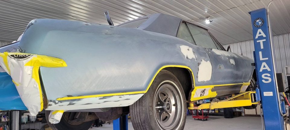 A classic convertible body in primer on the lift in the restoration bay