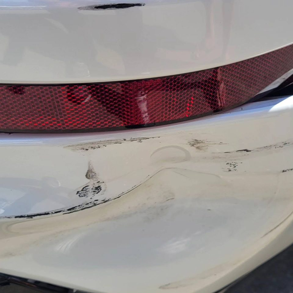 Collision damage — a crushed and scraped rear bumper on a white daily driver