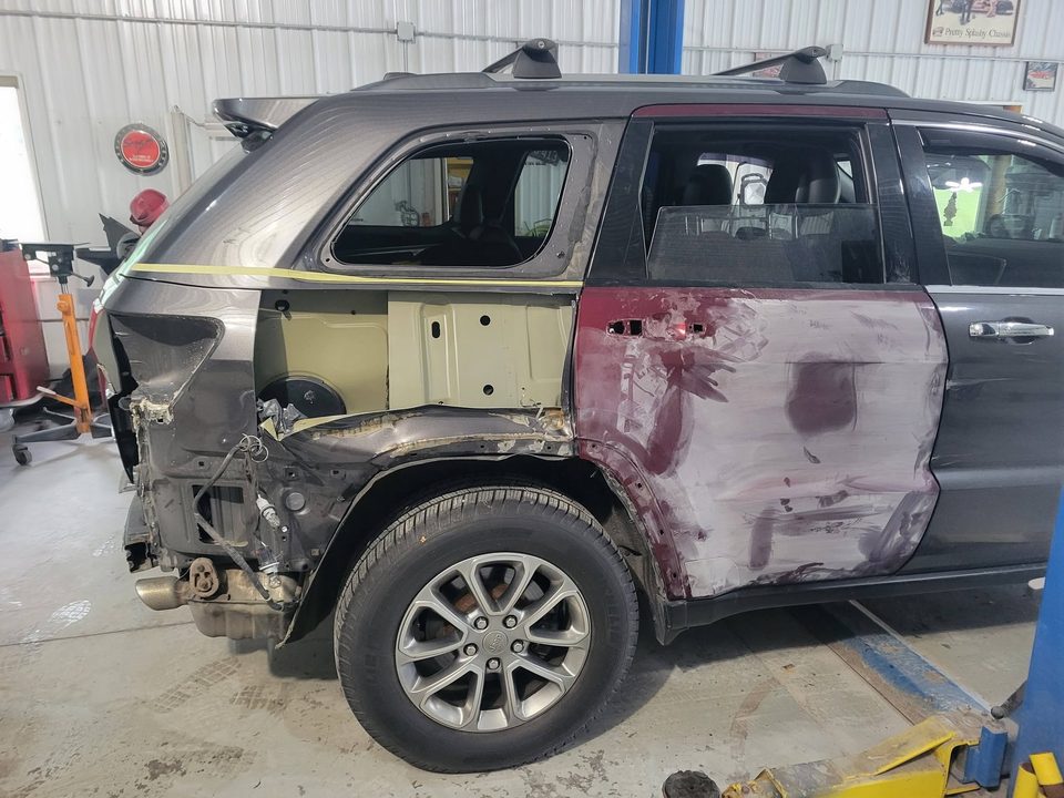 Collision repair in the body bay — rear quarter panel stripped and filled on a Jeep Grand Cherokee