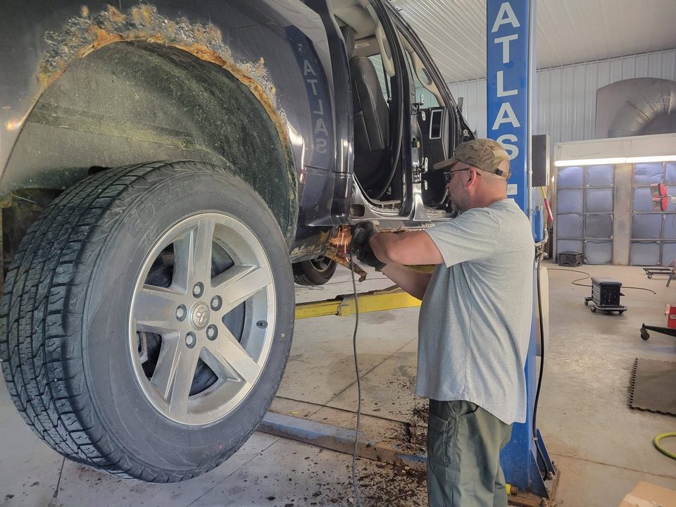 Technician working underneath a vehicle on the lift during structural repair